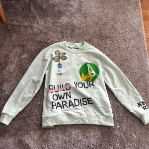 Ljusgrön sweatshirt från Zara med tryck - Cool ljusgrön sweatshirt från Zara med tryck framtill i flera färger och texten 'Build Your Own Paradise'. Rund halsringning och långa ärmar. Perfekt för en avslappnad stil.