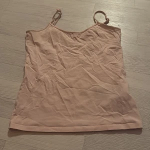 Beige/Rosa linnetopp med smala axelband - Enkel och stilren beige/rosa linnetopp med smala axelband. Toppen har rak passform och är tillverkad i mjuk bomull, perfekt för varma dagar eller som lager under andra plagg. Storlek XL men sitter som en S/M