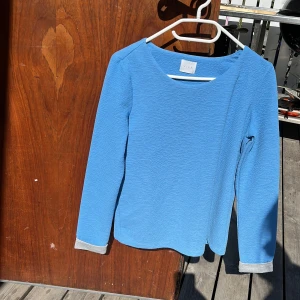 Blå långärmad tröja från Vila - En stilren blå långärmad tröja från Vila i storlek S. Tröjan har en rund halsringning och grå muddar vid ärmsluten som ger en snygg kontrast. Materialet är mjukt och lätt strukturerat, perfekt för lager-på-lager under kyligare dagar.