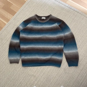 Randig stickad tröja från H&M - Säljer en stickad tröja från H&M i storlek 158/164. Tröjan har breda horisontella ränder i blått, grått och brunt med en rund halsringning och ribbade muddar. Perfekt för dig som gillar en chill och snygg look.