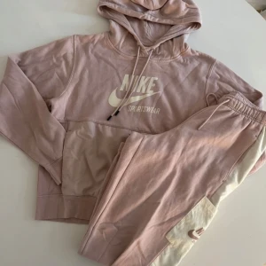 Fint rosa Nike set  - Nike hoodie i ljusrosa med vit logga på bröstet och snörning i huvan. Stor känguruficka framtill i ett glansigare material. Mjuk bomullskänsla, långärmad och relaxed fit. Perfekt för chill dagar eller träning. Tröjan har en brun prick på arm mudden som inte alls syns