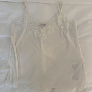 Vit spetslinnetopp med tunna band - Supersöt vit linnetopp med tunna axelband och vacker spetsdetalj upptill. Toppen har en liten fläck i mitten, därav de låga priset. Fläcken går säkert bort i tvätten❣️❣️