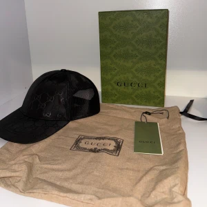 Svart keps från Gucci med GG-mönster - Snygg svart keps från Gucci limited edition med klassiskt GG-monogram över hela framsidan. Kepsen har mesh på sidorna och bak för extra ventilation samt justerbar snapback. Tillverkad i polyester och bomull, perfekt för en trendig streetstyle-look. Pris kan diskuteras! Storlek M 57cm (även justerbar). Använd fåtal gånger. 