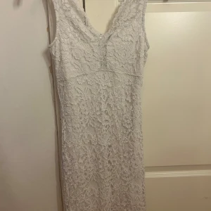 Vit spetsklänning från Cubus, stl 36 - Supersnygg vit spetsklänning med v-ringning och figurnära passform. Klänningen är ärmlös, har dragkedja i ryggen och vackert blommigt spetsmönster över hela. Perfekt för dig som vill sticka ut med en elegant look!