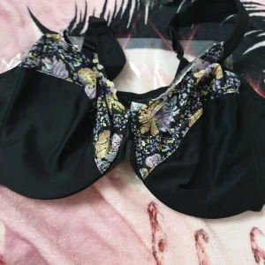 Svart blommig bh från Glamorise - Supersnygg svart bh från Glamorise med blommigt spetsmönster i lila, gult och beige upptill. Bh:n har bygel, breda axelband och en smidig knäppning framtill. Perfekt för dig som vill ha både stöd och en feminin look.