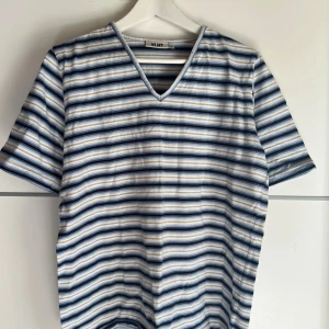 Randig t-shirt från XLNT KappAhl - Snygg t-shirt med v-ringning från XLNT by KappAhl. T-shirten har korta ärmar och ett randigt mönster i blått, beige, vitt och grått. Perfekt för dig som gillar en avslappnad och stilren look. Skön och mjuk känsla, passar till jeans eller shorts.