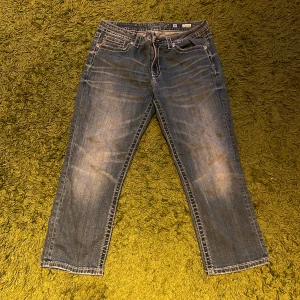 Boyfriend capri jeans med broderi - Snygga blå boyfriend capri jeans från Miss Me med slitningar och broderade detaljer på bakfickorna. Jeansen har raka ben och klassisk femficksdesign. Perfekta för en avslappnad och cool stil.