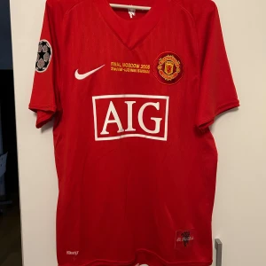 Manchester United Ronaldo 7 Finaltröja - Säljer en ikonisk röd Manchester United fotbollströja från Champions League-finalen 2008 med Ronaldo 7 på ryggen. Tröjan har korta ärmar, broderat klubbmärke, Nike-logga och AIG som sponsor framtill. Tillverkad i lätt och ventilerande material.