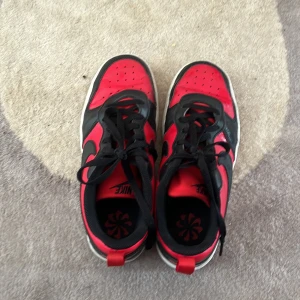 Nike Jordan 1 svart/röd sneakers - Säljer ett par Nike Jordan 1 sneakers i svart och rött med klassisk design. Skorna har snörning, rund tå och röd yttersula. Perfekta för dig som gillar streetstyle och vill sticka ut med en ikonisk modell.