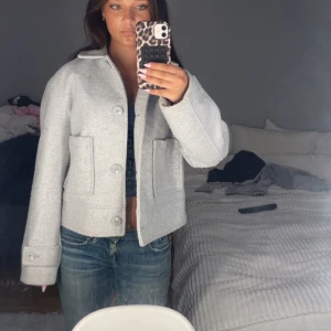 Ljusgrå kappa - Säljer en stilren ljusgrå jacka från lager 157, Jackan är croppad med stora knappar framtill, klassisk krage och två fickor. Perfekt till jeans och sneakers för en clean look. Långärmad och med snygga sömdetaljer. Bara att dm:a vid frågor eller funderingar!💕😊
