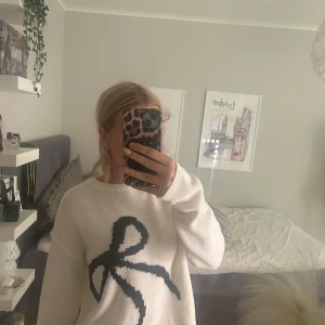 Vit stickad tröja med svart rosett - Superfin vit stickad tröja med en stor svart rosett framtill. Finns ingen lapp kvar så vet ej vart den är ifrån.
