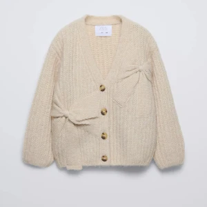 Beige stickad kofta med rosetter Zara - Superfin beige stickad kofta från Zara med v-ringning, stora knappar och två dekorativa rosetter framtill. Koftan har lång ärm och en mysig, lite oversized passform. Perfekt att slänga över en klänning eller till jeans för en chill look. (Pris går att diskuteras)❣️