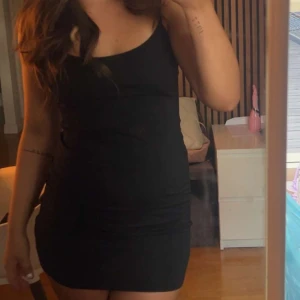 Svart tight kortklänning - Säljer en svart tight kortklänning med smala axelband och figurnära passform. Enkel och stilren design som framhäver siluetten. Perfekt för dig som gillar minimalistisk stil.