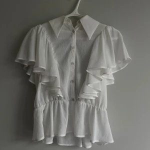 Elegant vit blus med volanger - En jättefin blus ifrån Zara, som har volanger och svart band som man kan knyta på olika sätt.                                     Blusen är knappt använd och är i superbra skick!    🤍