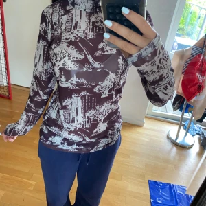 Brun långärmad polotröja med stadsmotiv - Säljer en brun långärmad polotröja med unikt vitt stadsmotiv. Tröjan är tight i modellen och har hög hals. 