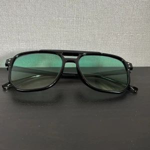 Solglasögon med grön tint  - Snygga solglasögon med klassisk pilotform och svarta bågar i plast. Glasen är gröntonade och ger en cool retrovibe. Perfekta för dig som vill sticka ut med en stilren accessoar till sommaren. Hör av dig vid minsta fundering!🤩💯 diskutera pris vid snabb och enkel affär👑👑