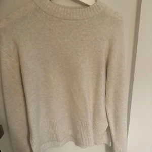 Beige stickad tröja från Kappahl XS - Mysig beige stickad tröja från Kappahl i storlek XS. Tröjan har ribbade muddar, rund halsringning och en liten slits i sidan. Perfekt för lager-på-lager och chill höst- eller vinterstil.