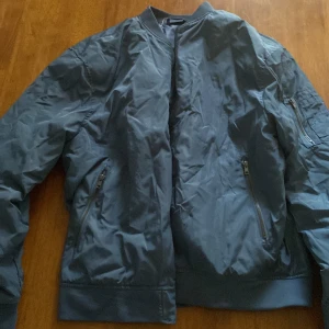 Blå bomberjacka från Livergy XL - Snygg blå bomberjacka från Livergy i storlek XL. Jackan har klassisk bombermodell med ribbade muddar, dragkedja framtill och fickor med dragkedja. Tillverkad i lätt polyester som passar perfekt för vår och höst. Enkel och stilren design som funkar till det mesta.