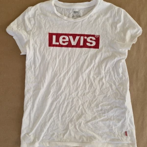 Vit Levi's T-shirt - T-shirt med röd logga från Levi's 🔥 Herrmodell i storlek XS, passar även dam S. 100% bomull. Finns ett mycket litet hål på sidan, se bilder. I övrigt är den i perfekt skick!  Pris är självklart förhandlingsbart :) Hör gärna av er vid frågor och glöm inte att kolla in garderoben för fler liknande plagg, jag samfraktar gärna! 💕