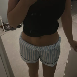 Randiga blåvita shorts med rosett - Säljer ett par söta shorts med blå och vita ränder, elastisk midja och svart rosett framtill. De har svarta detaljer längs bensluten och är perfekta för chill dagar hemma. Lätta och sköna med loose fit. Aldrig använt💕