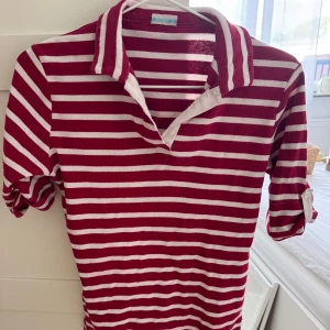 Randig rödvit pikétröja med krage - Pikétröja i rött och vitt med ränder och klassisk krage. Tröjan har halvkort ärm med knappdetalj för uppvik och är gjord i mjuk bomull. Perfekt för en chill och sportig look. (Säljer tröjan vidare så sista bilden är från förra säljaren) 👚🤍