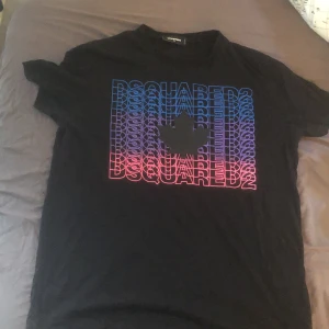 Svart DSQUARED2 t-shirt XL - Svart t-shirt från DSQUARED2 i storlek XL med färgstark print framtill i blått, lila och rosa med DSQUARED2-logga och lönnlöv. Klassisk passform och rund hals. Perfekt för dig som gillar streetstyle och vill sticka ut med en snygg logga.