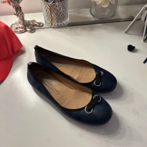 Mörkblå ballerinaskor Marc Jacobs - Snygga mörkblå ballerinaskor från Marc Jacobs i skinn med rund tå. Dekorativa svarta rosetter framtill med silvriga metalldetaljer. Platt sula med cirkelmönster undertill. Perfekta för dig som gillar klassisk och stilren design.