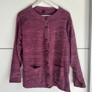 Lila kofta från Mai-ly med knappar - Säljer en lila kofta från Mai-ly i storlek L. Koftan är stickad med ett randigt mönster i olika nyanser av lila och har snygga matchande knappar framtill. Två praktiska fickor framtill och långärmad modell. Perfekt för lager-på-lager under kyliga dagar.