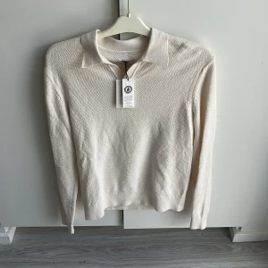 Beige pikétröja från These Glory Days - Snygg beige pikétröja från These Glory Days i ekologisk bomull. Tröjan har klassisk krage, lång ärm och diskret strukturstickat tyg. Perfekt för dig som gillar stilrena och enkla plagg med en modern touch. Nu med prislapp kvar. Köparen står för frakt!