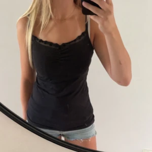 Svart linnetopp med spetskant - Snygg svart linnetopp med smala axelband och fin spetskant upptill. Toppen har en figurnära passform och är perfekt för varma dagar eller som lager under en skjorta. Enkel och stilren design som passar till det mesta.