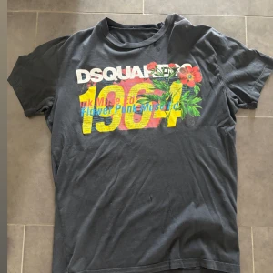 Svart DSQUARED2 t-shirt med tryck - Cool svart t-shirt från DSQUARED2 med färgglatt tryck framtill, stora siffror, blommor och text. Klassisk passform och rund hals. Perfekt för dig som gillar statement-plagg och streetstyle.
