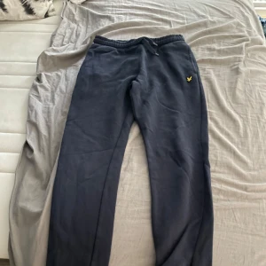 Mörkblå mjukisbyxor Lyle & Scott Junior - Mörkblå mjukisbyxor från Lyle & Scott Junior med resår och snörning i midjan. Byxorna har en bakficka och den klassiska gula loggan broderad framtill. Perfekta för chill eller träning, riktigt sköna och stilrena.