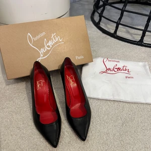 Svarta klackar från Christian Louboutin - Klassiska svarta klackar från Christian Louboutin i skinn med ikonisk röd sula och spetsig tå. Insidan är röd med guldfärgad logga. Snygg och tidlös modell med smal klack som ger en elegant look.