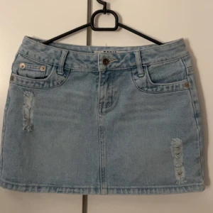 Söt ljusblå jeanskjol med slitningar - Säljer en ljusblå jeanskjol från BASIC med slitna detaljer framtill och klassiska fickor både fram och bak. Kjolen har bälteshällor och knappstängning i midjan. Perfekt för dig som gillar en chill och trendig look. Köptes i Thailand på chatuchak bangsue junction! 