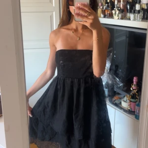 Svart volangklänning utan band  - Supersöt svart axelbandslös klänning med voluminös kjol och broderade spetsdetaljer nertill. Säljer tyvärr eftersom den är för stor (strl 36)