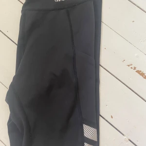 Svarta leggings från Stronger, S - Svarta leggings från Stronger i stretchigt material med snygga vita reflexdetaljer på benen. Mobilficka på båda benen!