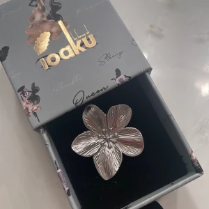 Blommig silverring från Ioaku - Statementring från Ioaku i silverfärgad metall, formad som en stor blomma med fem detaljerade kronblad. Ringen har justerbar öppning baktill så den passar flera storlekar. Perfekt accessoar för dig som vill sticka ut med en cool och unik look.