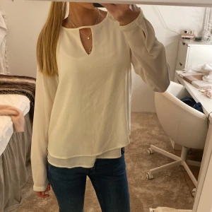 Vit blus med volang  - Säljer en stilren vit blus med långärmade, lätt transparenta ärmar och en snygg nyckelhålsringning framtill. Blusen har en lös passform och dubbla lager tyg nedtill för en extra snygg look. Perfekt att matcha med jeans eller kjol. Kan behöva strykas