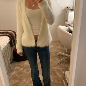 Vit fluffig cardigan jacka Gina Tricot - Supermjuk och fluffig vit cardigan jacka från Gina Tricot. Långärmad, öppen framtill och med två stora fickor. Stickad i ett lurvigt material som känns extra cozy och chill. Perfekt att slänga på sig över en topp för en avslappnad look.