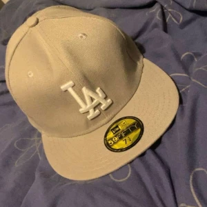 Beige LA Dodgers keps New Era 59FIFTY - Snygg beige LA Dodgers keps från New Era 59FIFTY med broderad LA-logga framtill och 1988 World Series-detalj på sidan. Klassisk rak skärm och broderade loggor i vitt. Perfekt för dig som gillar streetwear och sportig stil.