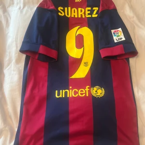 Äkta Luis Suarez Fc Barcelona tröja Nike nr 9 - Säljer en väldigt snygg och sällsynt Nike Fc Barcelona tröja från säsongen de vann Champions League 2014/15 med legendaren Luis Suarez nr 9 på ryggen! Köpt på camp nou! Tröjan är i storlek S och är i väldigt fint skick! Den ända lilla skadan som finns är att numret har blivit lite skrynkligt. Syns knappt men vill bara vara ärlig!  Hör av dig vid minsta lilla fundering och kolla gärna in mina andra annonser med bland annat andra fotbollströjor!