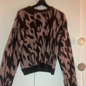 Stickad leopardmönstrad tröja - Säljer en stickad tröja med leopardmönster i svart och beige/rosa i storlek S. Tröjan har en loose passform och långa ärmar, perfekt för dig som vill ha en trendig och bekväm look. Mjuk och skön att bära, passar till många olika outfits. Lite nopprig. Pris kan diskuteras🥰