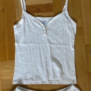 Vit linne med små rosa hjärtan - Supersöt vit linne från Brandy Melville med små rosa hjärtan över hela tyget. V-ringad framtill med tre dekorativa knappar och smala axelband. Perfekt för varma dagar eller som pyjamastopp💞🎀
