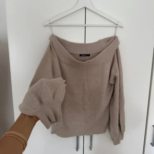 Beige stickad offshoulder-tröja Glamorous - Supermysig beige stickad tröja från Glamorous med bred offshoulder-ringning och långa ärmar. Tröjan har ribbade muddar och en loose fit som ger en chill vibe. Perfekt att styla med jeans eller kjol för en trendig look.
