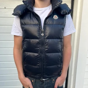 Moncler Vest - Säljer min i princip helt nya Moncler Vest i färg: Svart ⚫️. Perfekt för dig som vill ha en skön väst till sommaren, Storlek: 2 (Medium). Helt fri från defekter och väldigt fin till många outfits. 🌺 OBS〽️. Äktighet kan ej bekräftas har därför lagt till bilder på carton och NFC Tag funkar perfekt. Man får ta reda på om det är riktigt eller inte. Men den är köpt som äkta!🎉  Priset är EJ hugget i sten och kan diskuteras vid trevlig affär! Hör av er vid minsta lilla fundering!‼️✅🌊