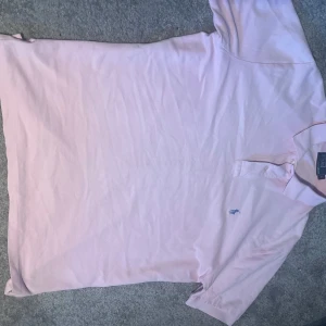 Ljusrosa pikétröja från Ralph Lauren - Säljer en klassisk ljusrosa pikétröja från Ralph Lauren med blå broderad logga på bröstet. Tröjan har korta ärmar, krage och två knappar vid halsen. Den passar dig som vill se extra snygg till sommaren.  När jag fick den då var den för stor men säljer vidare till nån som behöver 