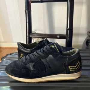 Valentino Rockrunner svarta sneakers - Svarta Phillipe Model sneakers i mocka och skinn med Gulag detaljer. Snygga broderade chevron-märken på hälen och gula stjärnor på plösen. Klassisk rund tå, snörning och vit sula. Perfekta för dig som gillar streetstyle med lyxig touch.