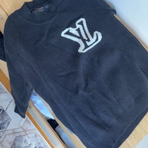 Svart stickad tröja Louis Vuitton - Svart stickad tröja från Louis Vuitton med stort vitt LV-logo framtill. Klassisk rund halsringning och ribbade muddar vid ärmslut och nederkant. Perfekt för dig som vill ha en lyxig och stilren look med streetkänsla. Säljs endast för 1300kr kom gärna med bud!