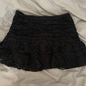 Svart kortljol med volanger och spets - Svart kortkjol från NA-KD med blommig spets och volanger. Kjolen har dragkedja på sidan och sitter snyggt i midjan. Använd 2 gånger!!