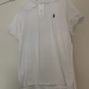 Vit pikétröja Polo Ralph Lauren S - Vit pikétröja från Polo Ralph Lauren med klassisk krage, knappar och broderad logga på bröstet. Slim fit-modell i bomull som ger en clean och fräsch look. Perfekt för dig som gillar stilrena och tidlösa plagg.